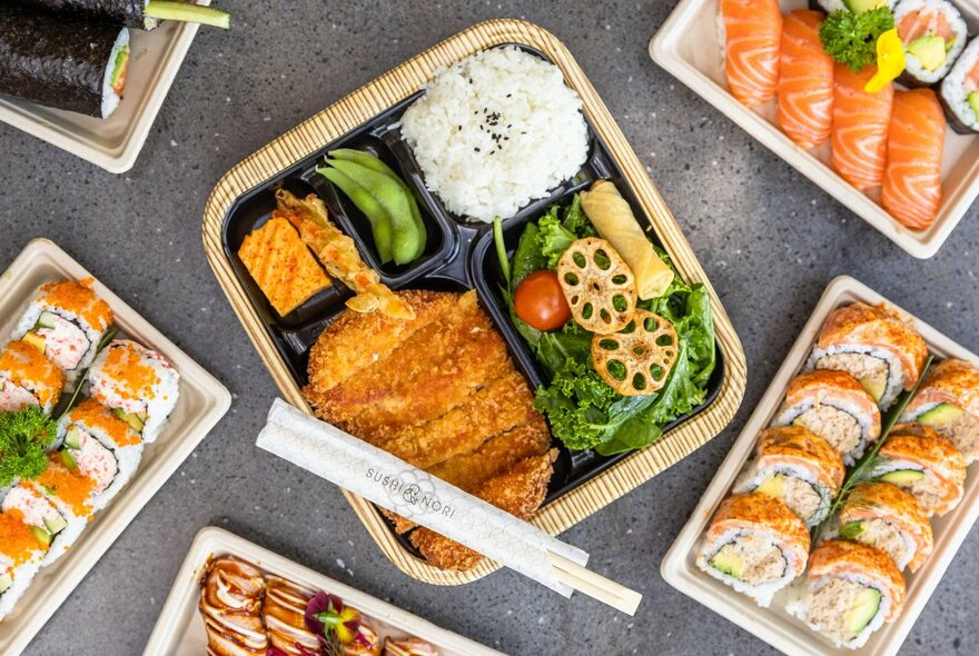 Overhead view of takeaway dishes of sushi and Japanese bento-style boxes.