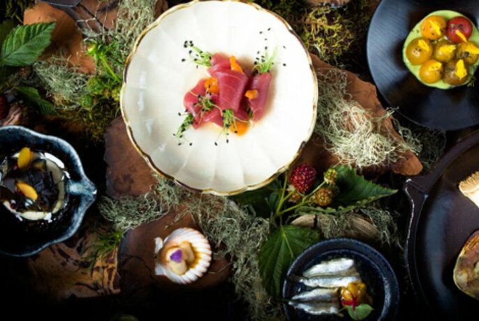 Overhead view of different sized plates of seafood and shellfish on wooden surface, decorated with leaves and herbs.