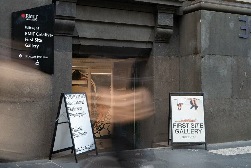 Building exterior of First Site Gallery at RMIT showing entrance and two sandwich boards on the footpath with signage related to the gallery.