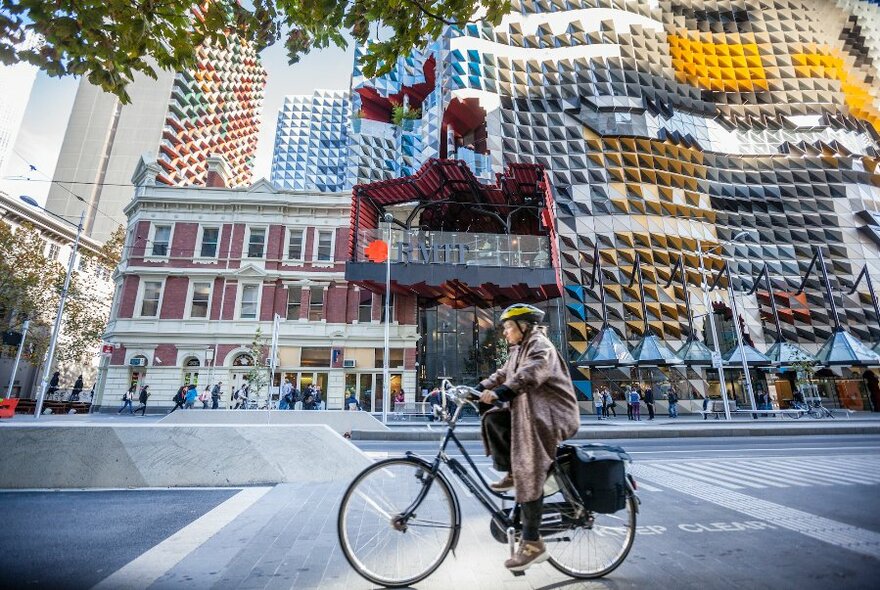 A cyclist riding past the colourful facade of RMIT.