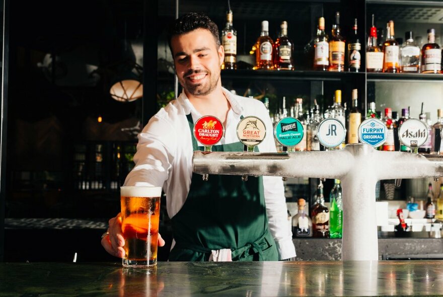 A bartender placing a glass of beer on a bar.
