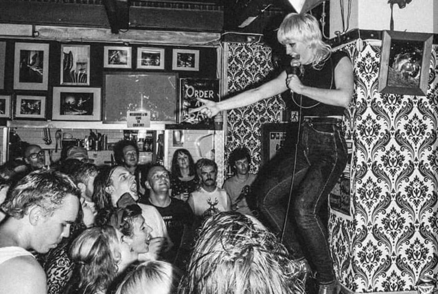 Woman singing on stage of Rock & Roll dive bar and packed audience dancing and singing along.