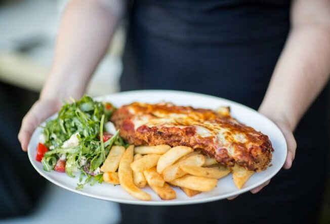 A chicken parma on a plate with chips and salad