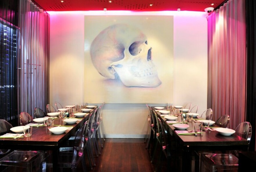 Two long restaurant tables and drawing of human skull hanging on the wall.