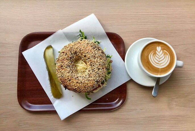 Filled bagel with a pickle the side on a tray, with a cup of coffee.