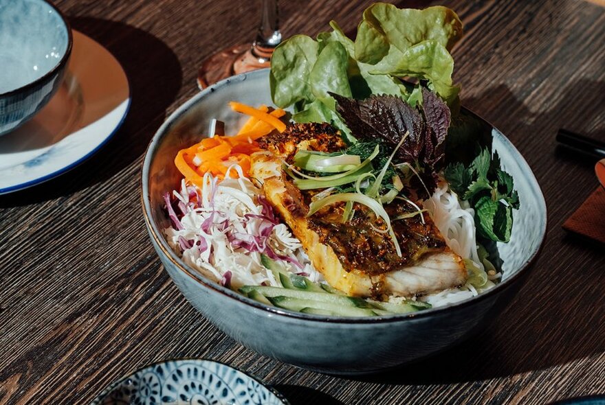 A Vietnamese dishe served in a bowl, topped with salad ingredients.