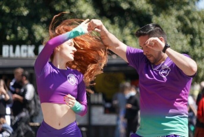 Two people dance vigorously in purple shirts outdoors.