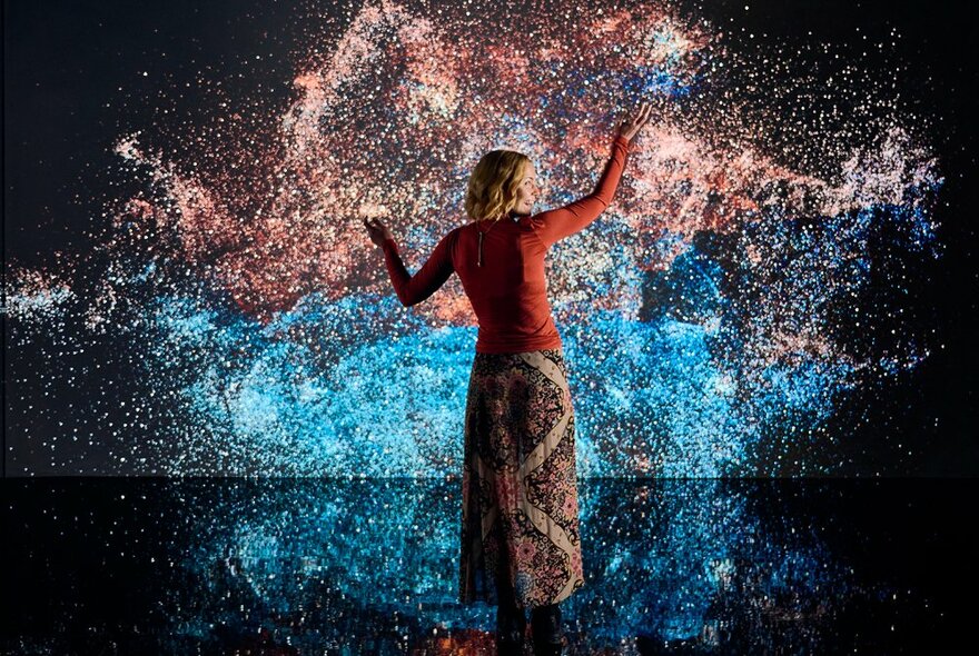 View of a person from behind, standing in front of a display of swirling cosmic patterns and colours on a wall.