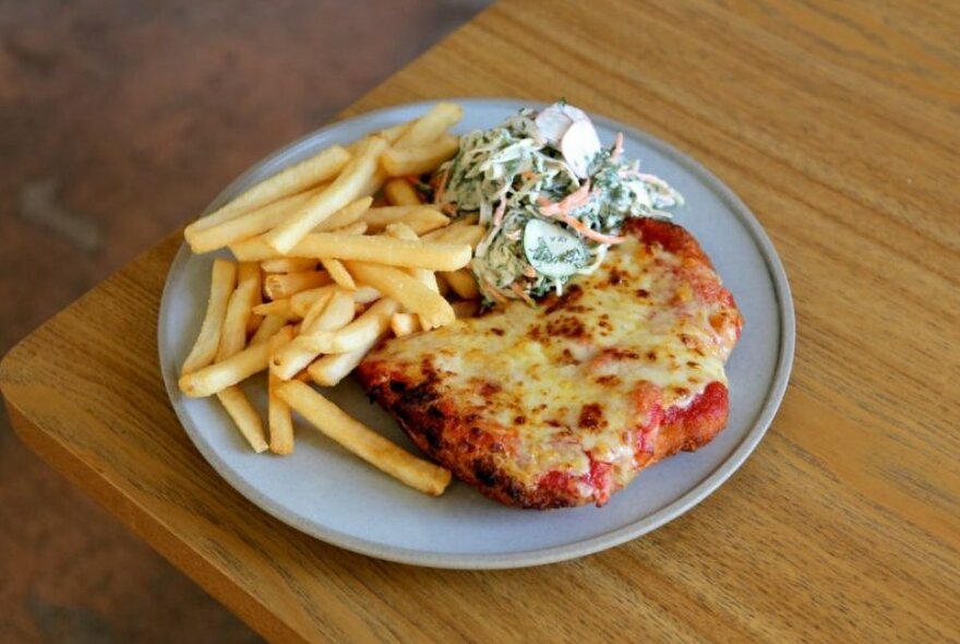 A chicken parma on a plate with chips and salad