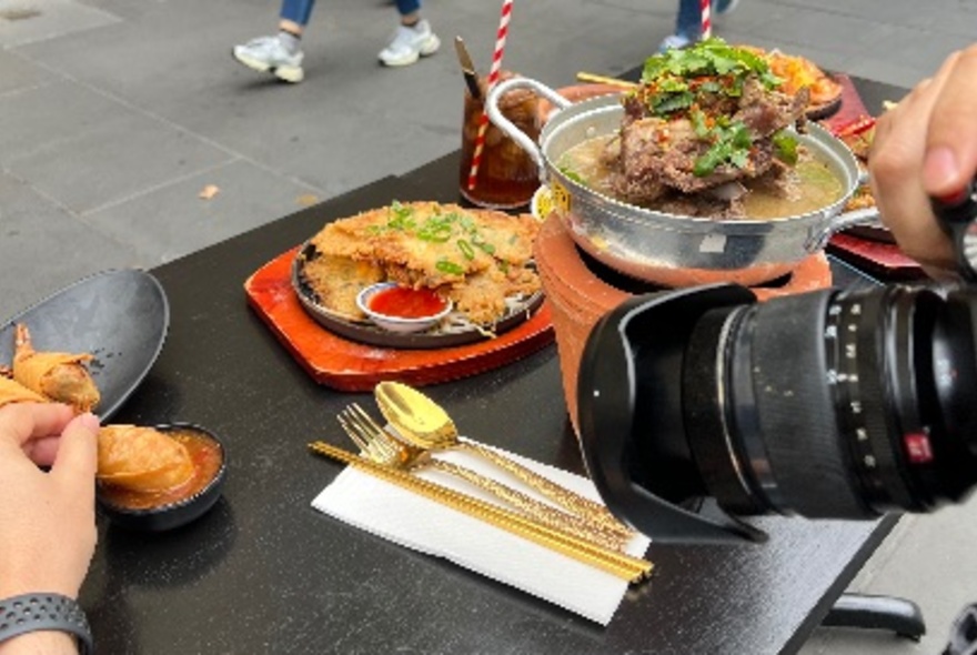 A selection of Thai-style dishes on a black table being photographed with a camera with large lens.