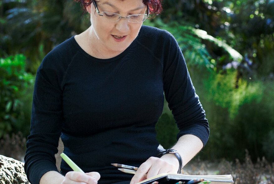 A person sketching outdoors, holding pencils and a sketchbook in their hands.