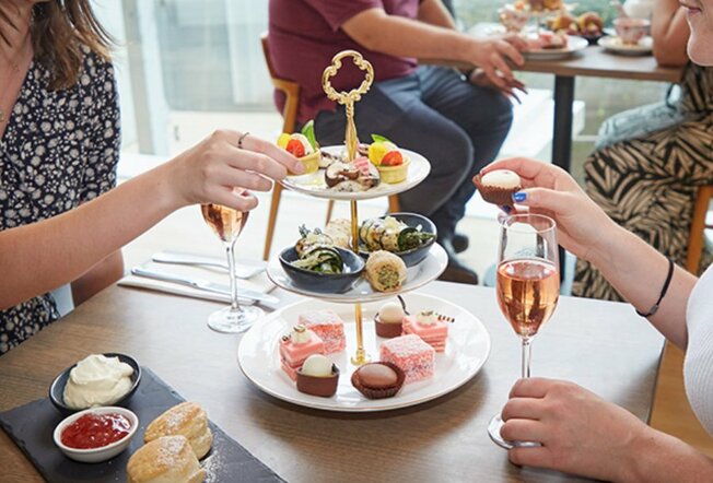 People drinking sparkling rosé and taking tiny sweets from a tiered tray. 
