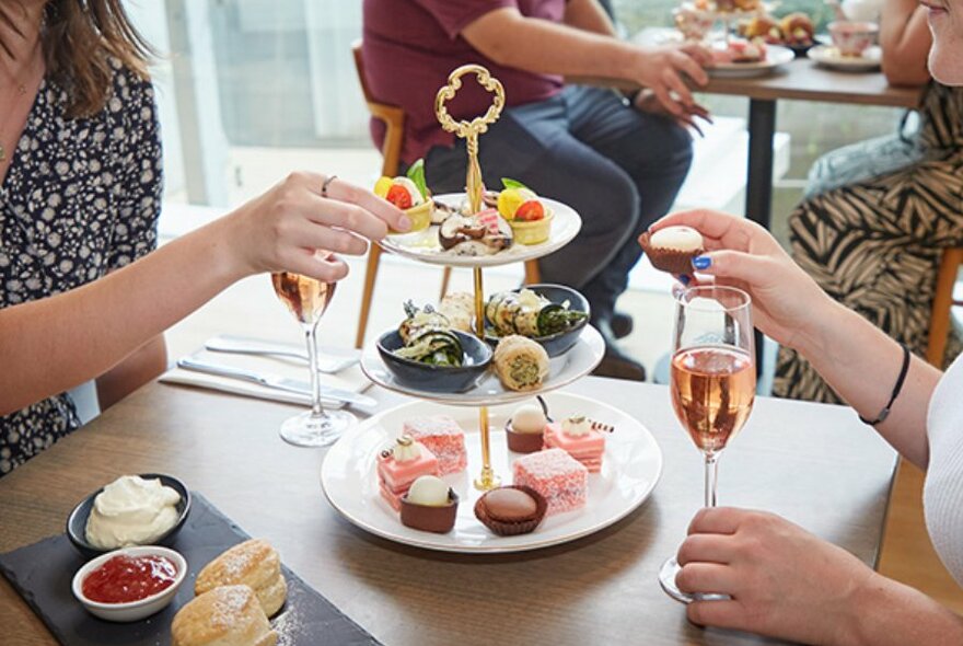 People drinking sparkling rosé and taking tiny sweets from a tiered tray. 
