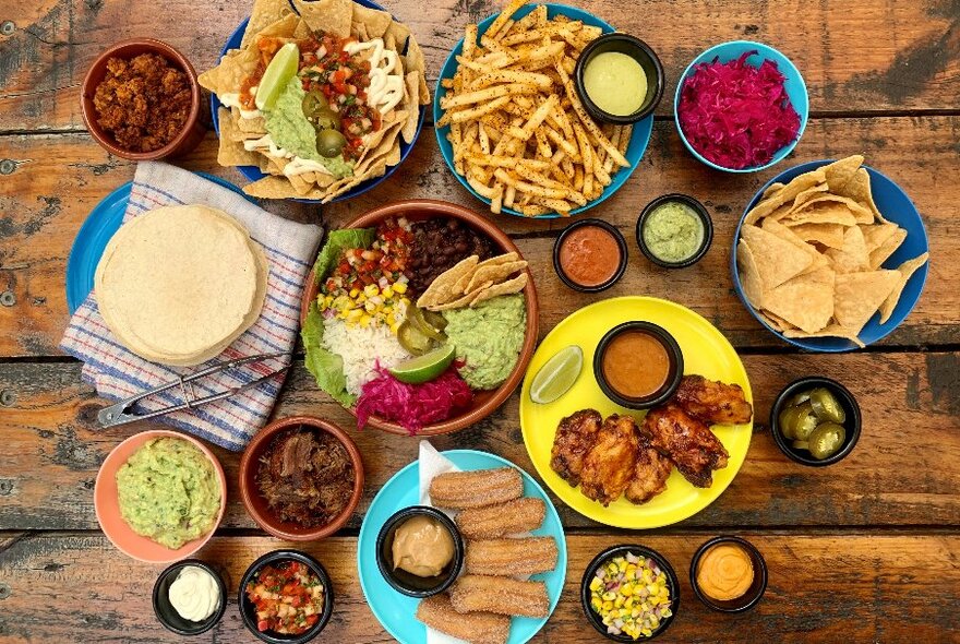 Overhead view of colourful plates of Mexican food including dips, chips and salsas.