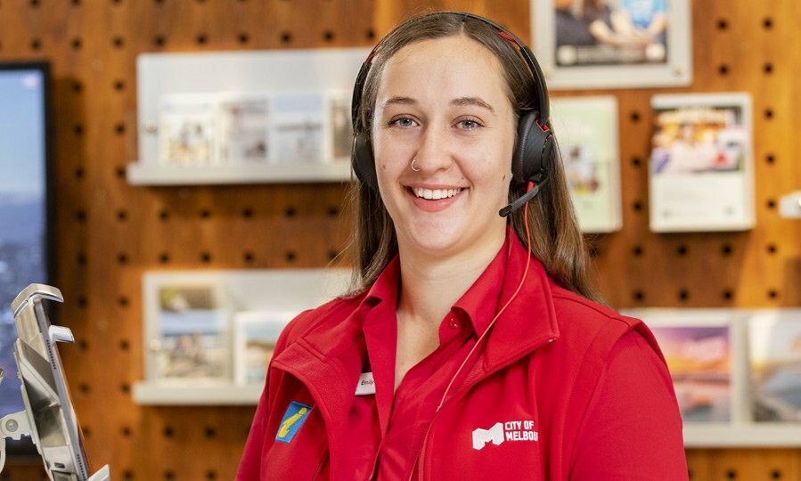 Smiling woman in Visitor Hub, wearing a headset and a red uniform.