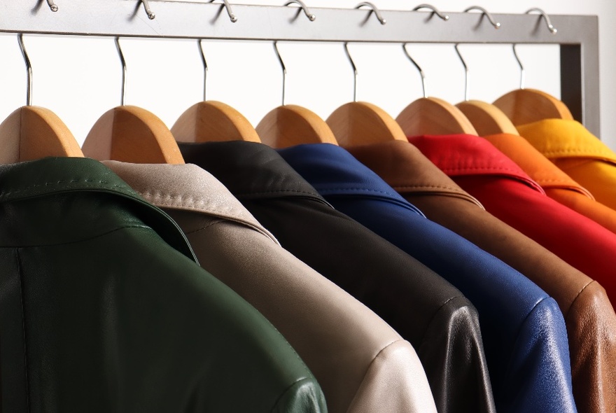 Solid coloured leather jackets on wooden hangers on a display rack in a store.