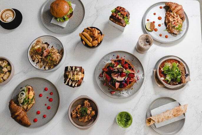 Overhead shot of Korean dishes on a white table, including burger, wraps and condiments.