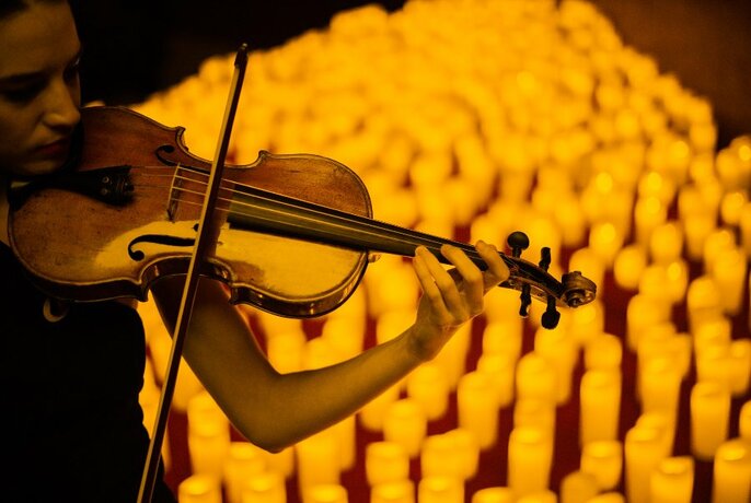 A violinist performing in front of an array of yellow candles.
