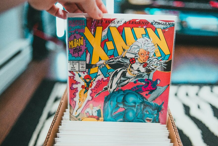 Someone picking an x-men comic book from a box of comics.