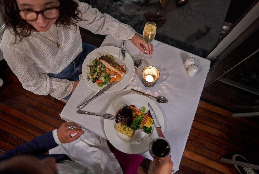 Looking down from above at a table for two with meals, wine and a tea-light candle. 