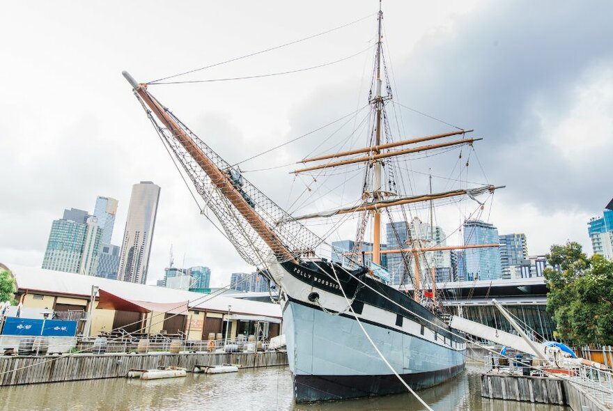 The Polly Woodside sailing vessel moored on the river with the Melbourne city skyline in the background.