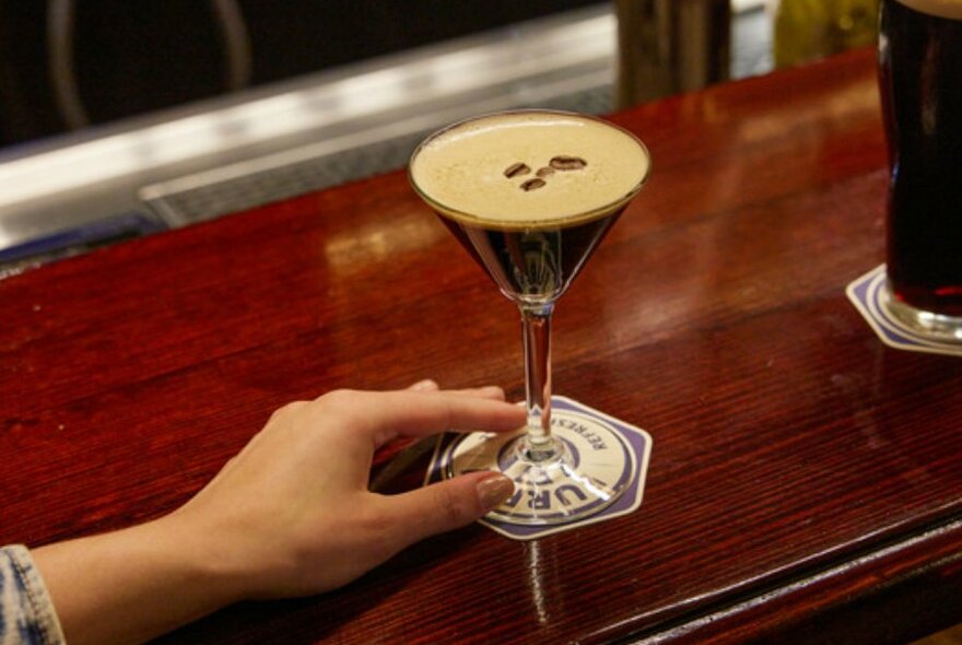 A woman's hand holding an espresso martini on a wooden bar.