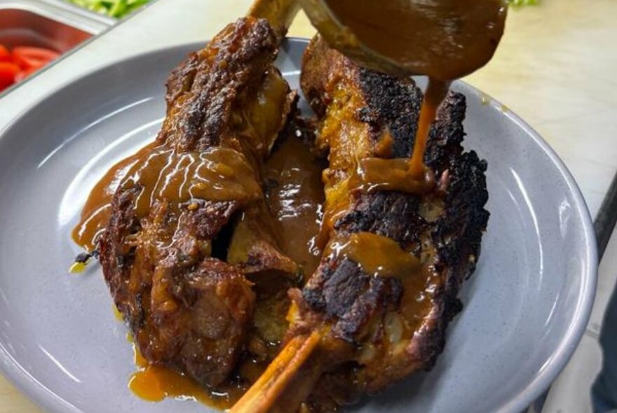 Barbecued meat on bone, on white plate, with gravy being poured on top.