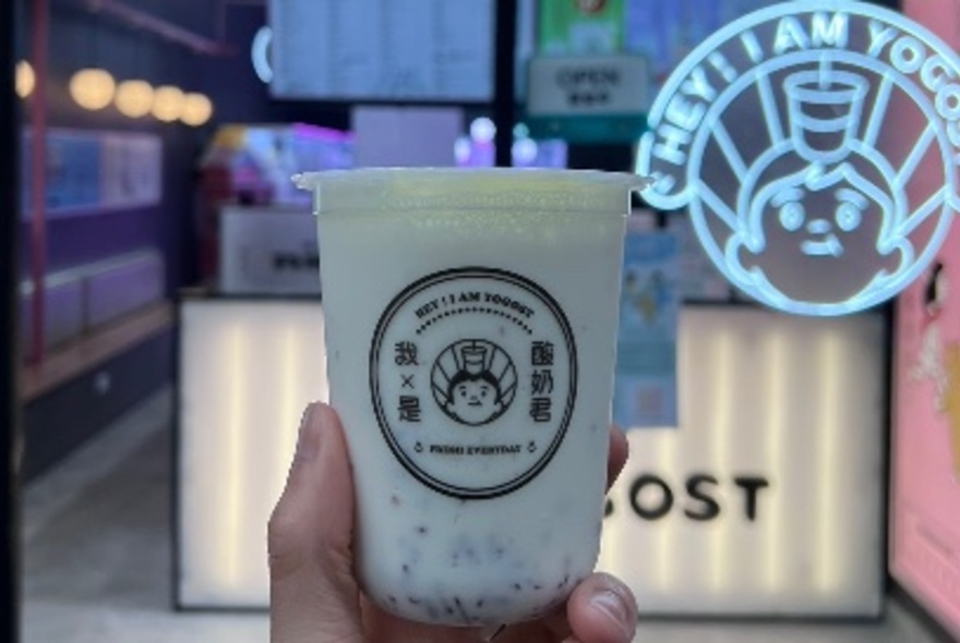 Hand holding a branded yoghurt cup with neon cafe in the background.