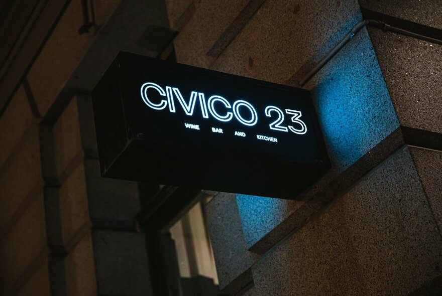 Softly lit signage with the words 'Civico 23' affixed to the exterior of a building.