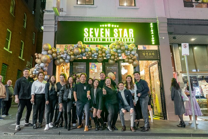 Large group of people standing out the front of a  Seven Star restaurant in a city street.
