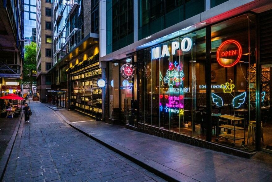 Exterior of Mapo restaurant with neon signs in windows, in a laneway, at dusk.