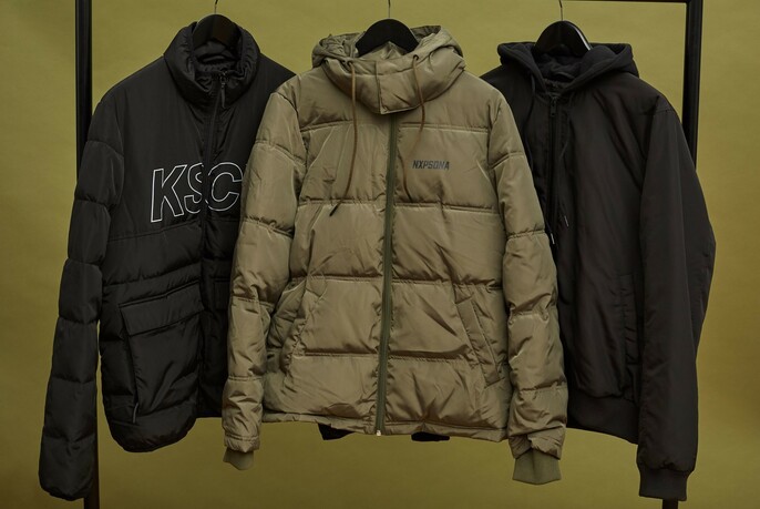 Three puffy jackets hanging on a rail against a khaki background.