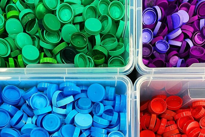 Different coloured plastic bottle tops sorted into trays for recycling.