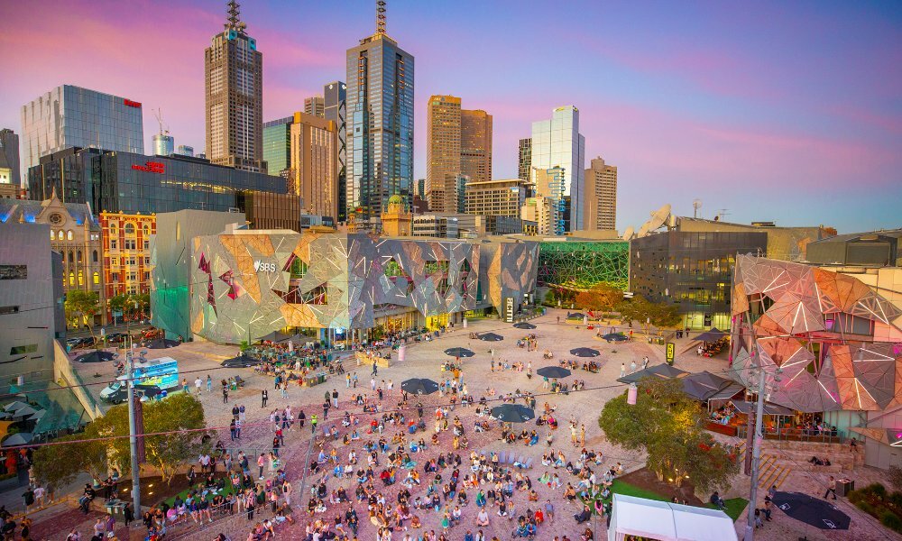 People milling around Fed Square at sunset.
