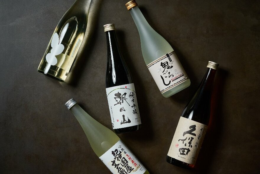 Four bottles of wine and sake arranged flat on a table surface, their labels showing.