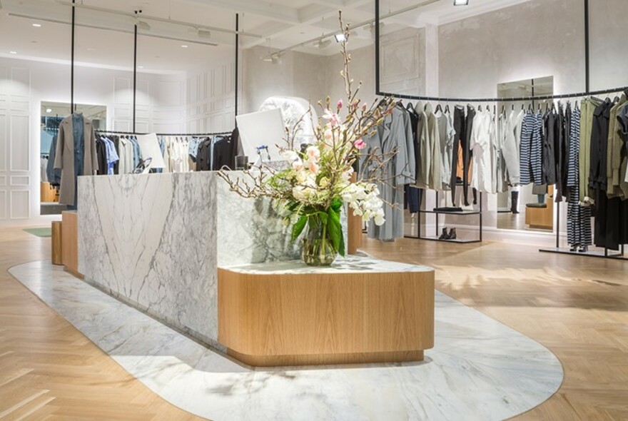 Camilla and Marc interior with racks of clothing surrounding a central marble sales desk with flowers.