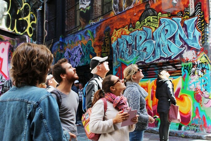 Group of people looking upwards at street art in Melbourne with graffitied laneway in background.