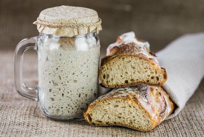 Glass jug filled with sourdough starter, next to sliced sourdough bread on a table.