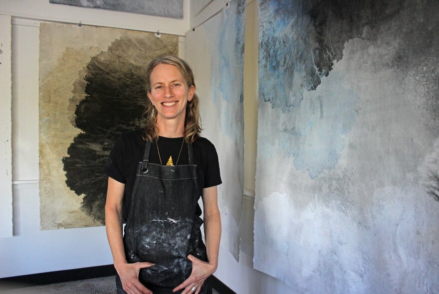 Artist Melinda Schawel wearing a black apron smiling in front of her work.