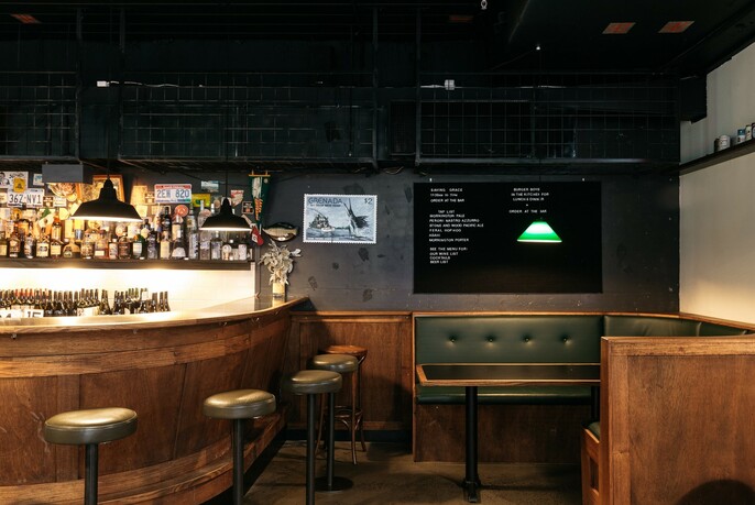 Darkly lit semicircular bar with stools and bench seating, pendant lighting and bottles.