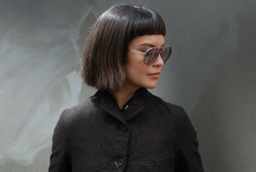 Model wearing a dark buttoned-up coat and sunglasses.