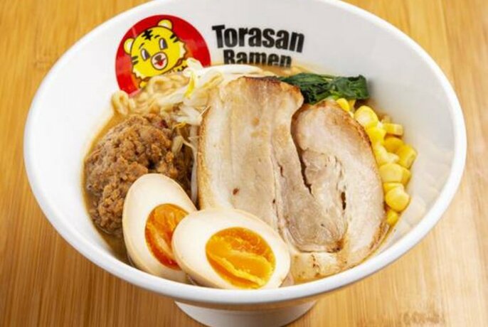 Bowl of ramen noodles with half boiled eggs, sweetcorn kernels and a slice of pork resting on the top.