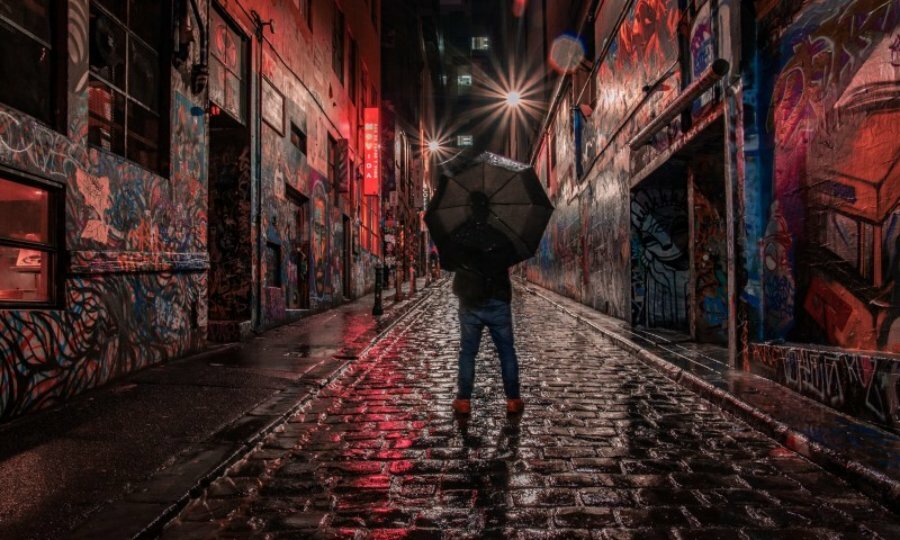 A person with an umbrella in graffiti-covered Hosier Lane on a rainy night.