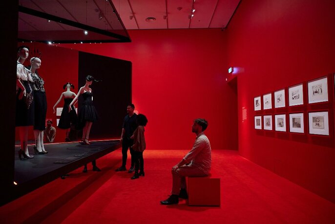 A red gallery space with people looking at dresses.