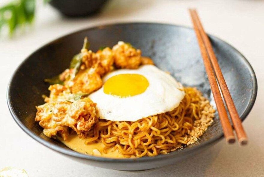 Noodles in a black bowl with a fried egg and fried chicken on top