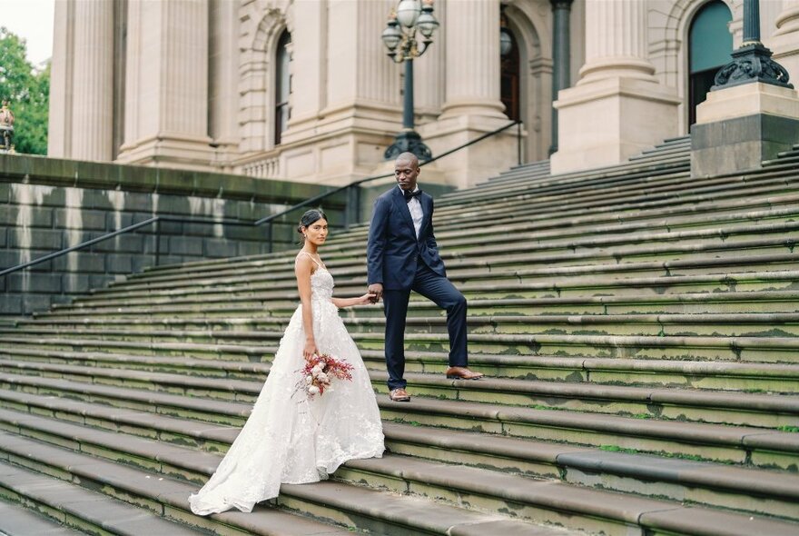 Bride and groom in wedding attire, posing for a photograph outdoors on a long flight of steps.