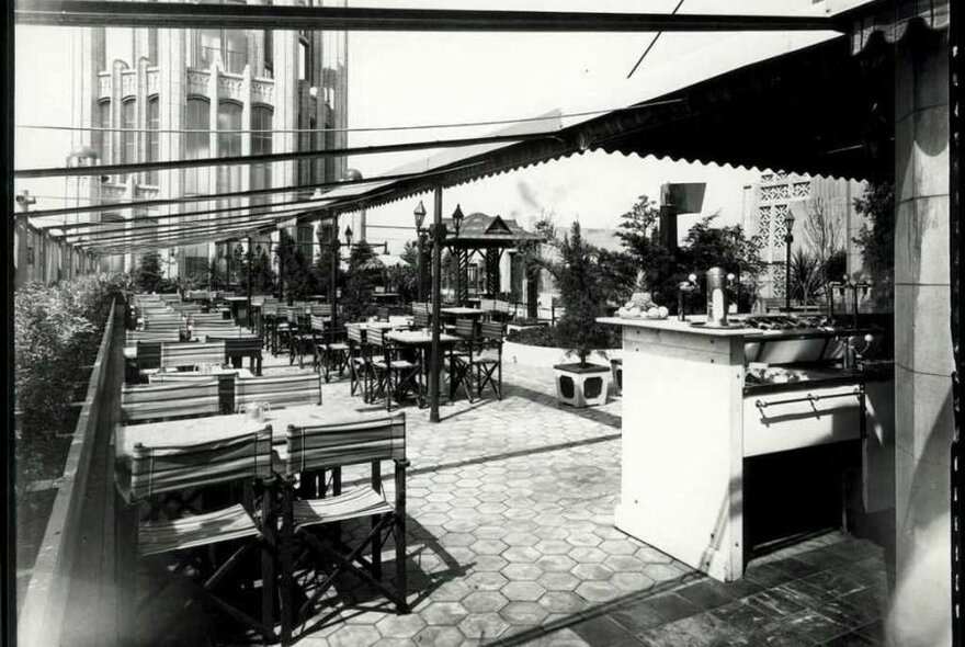 A black and white photo of an empty outdoor terrace at a cafe with dining tables 