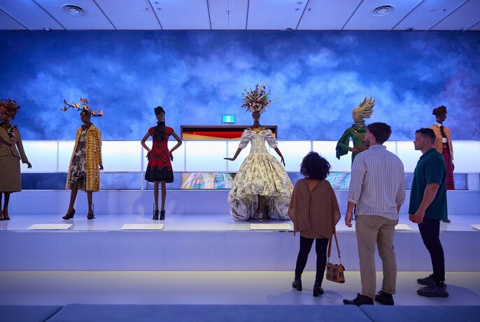 People looking at a gallery display of dramatic dresses in a blue room.