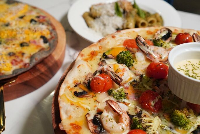 Close-up of a pizza with a topping of cherry tomatoes, small prawns and broccoli florets.  