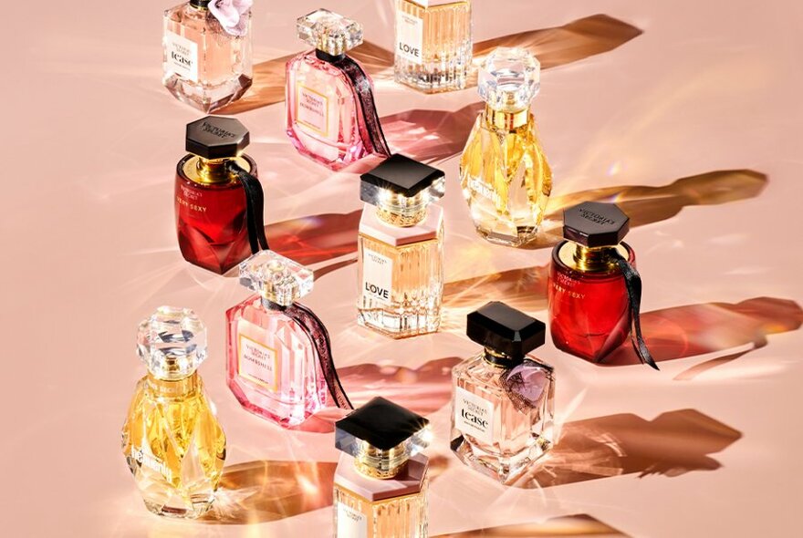 Perfume bottles on pink surface casting shadows.